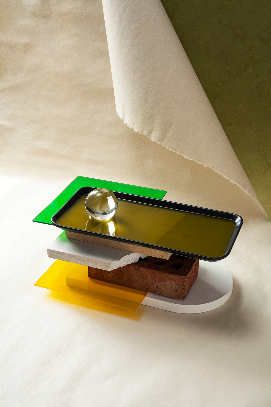 A balanced stack of a black tray, brick, concrete, and colored glass — expertise held in balance by structure.
